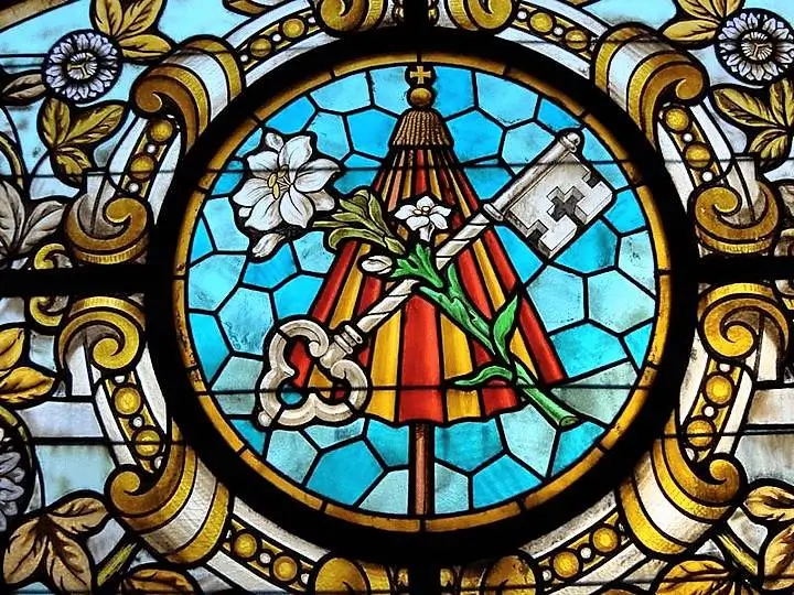 La imagen muestra un vitral con el escudo de armas del Papa Francisco. 
