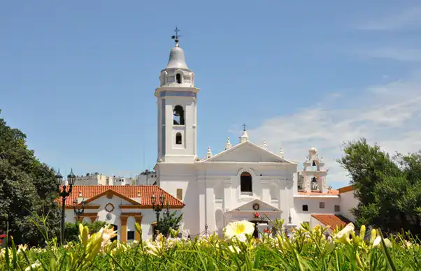 Catedral histórica en Buenos Aires con arquitectura colonial y campanario alto, rodeada de jardines verdes.